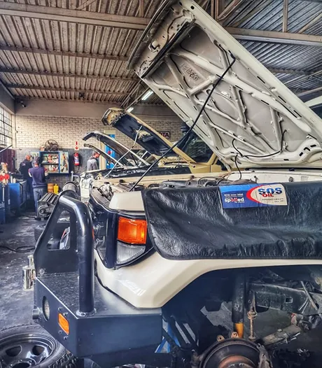 Mechanics at work behind a Land Cruiser with its bonnet raised