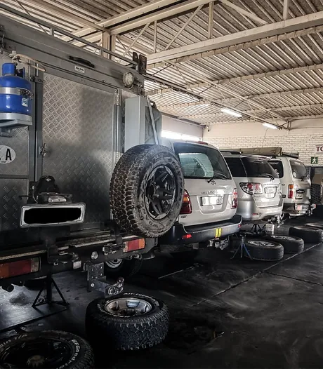 A touring camper body and a row of Land Cruisers on stands in the workshop