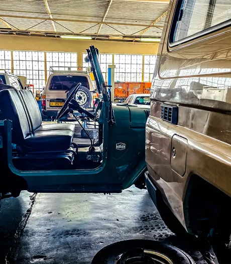 A classic open-top Land Cruiser parked beside a Troop Carrier in the workshop